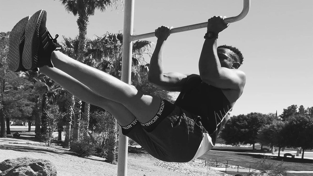 Person hanging from a bar by hands outdoors with trees in the background